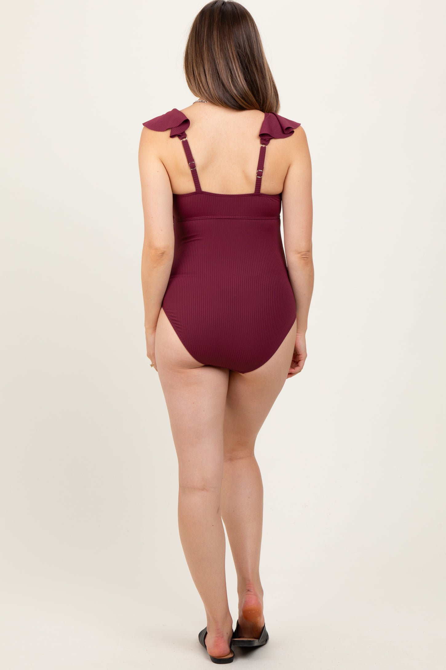 woman wearing a burgundy ribbed one-piece maternity swimsuit with ruffled straps and a low back, no visible baby bump