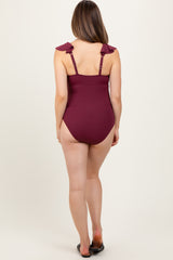 woman wearing a burgundy ribbed one-piece maternity swimsuit with ruffled straps and a low back, no visible baby bump