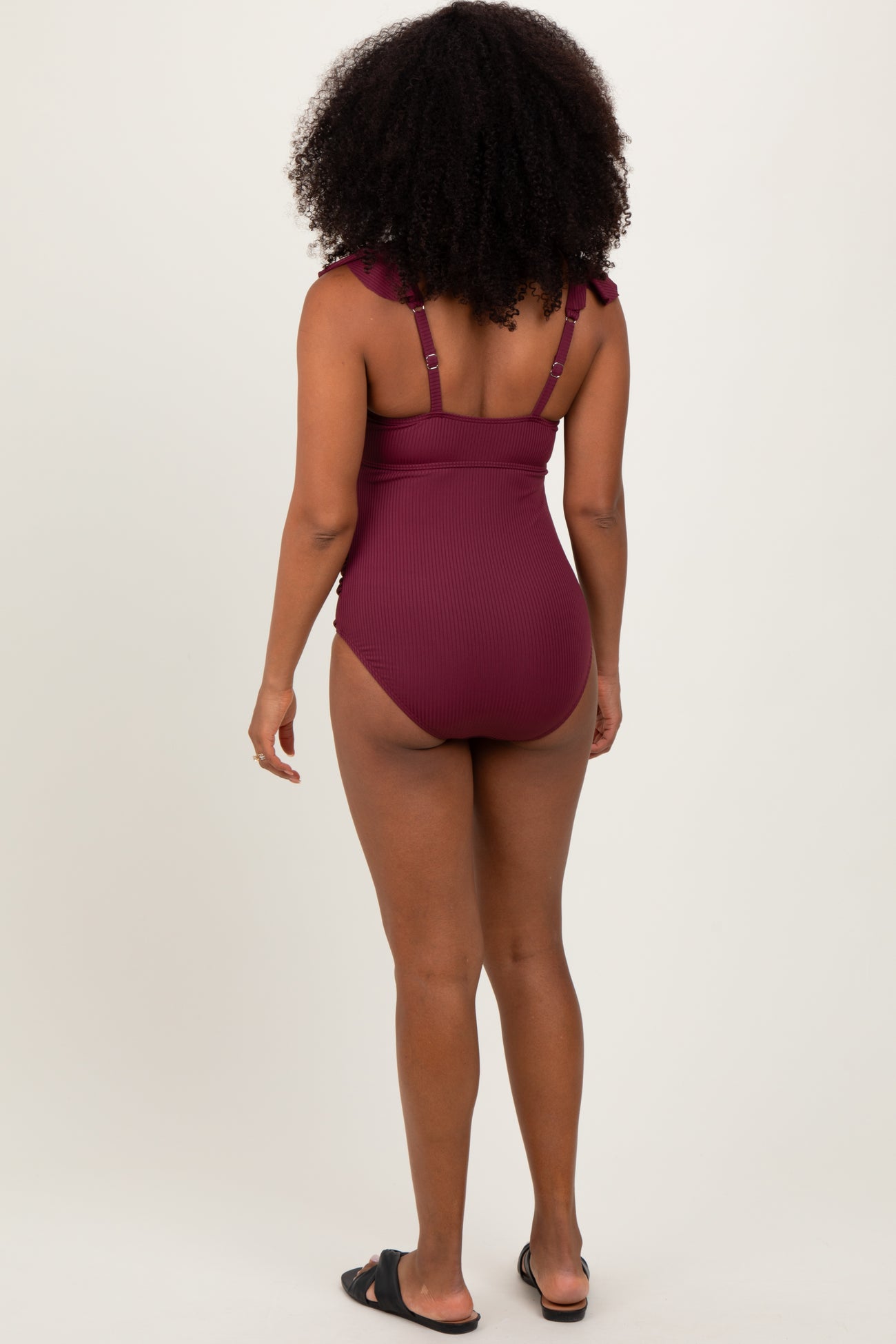 woman wearing a burgundy ribbed one-piece swimsuit with ruffle straps, viewed from the back