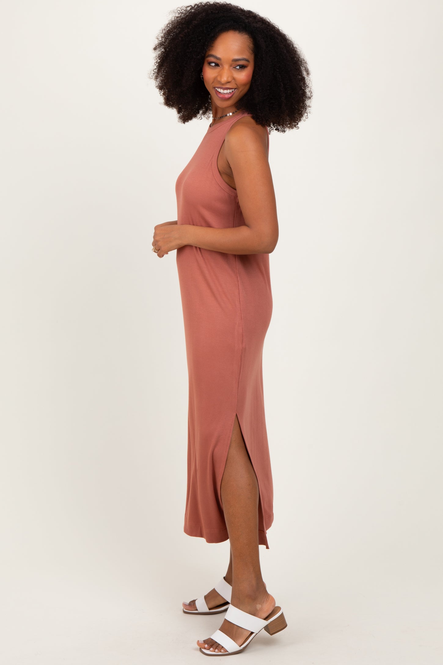 woman wearing a rust-colored sleeveless maxi dress with side slits and standing sideways with a relaxed pose