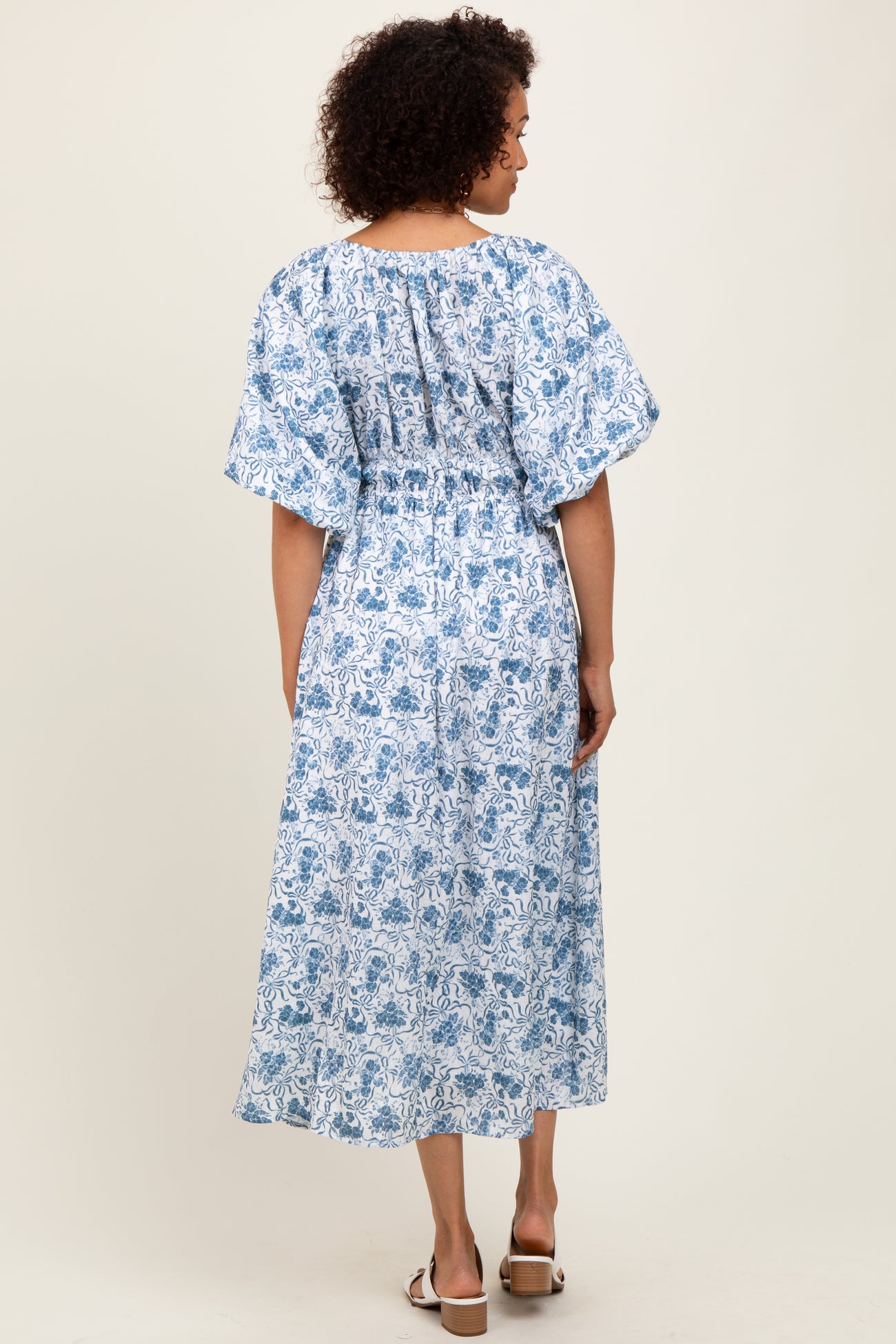 woman wearing a blue and white floral maxi dress with short flutter sleeves and a smocked bodice, viewed from the back