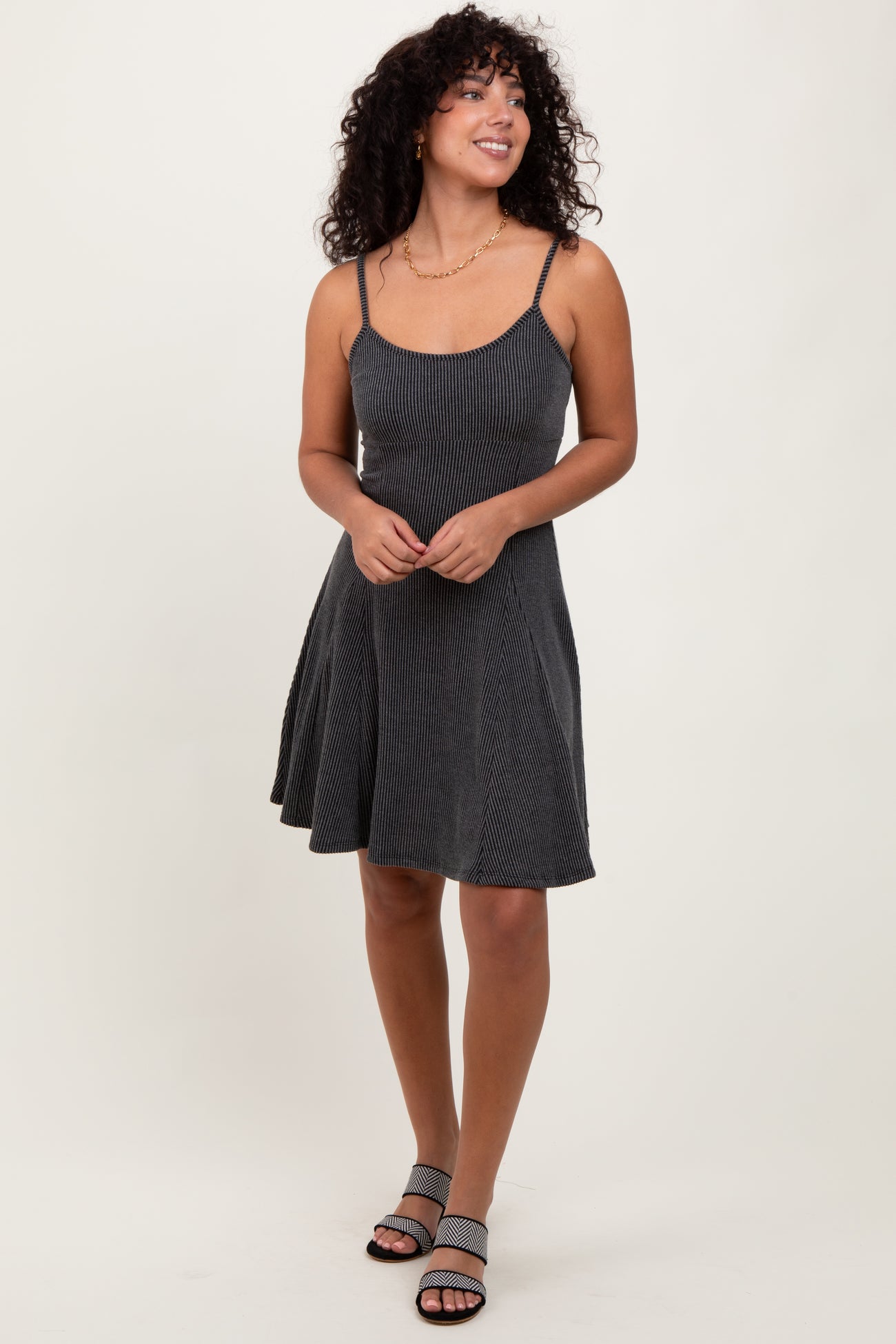 woman wearing a black and white striped spaghetti strap dress with a flared skirt and strappy sandals