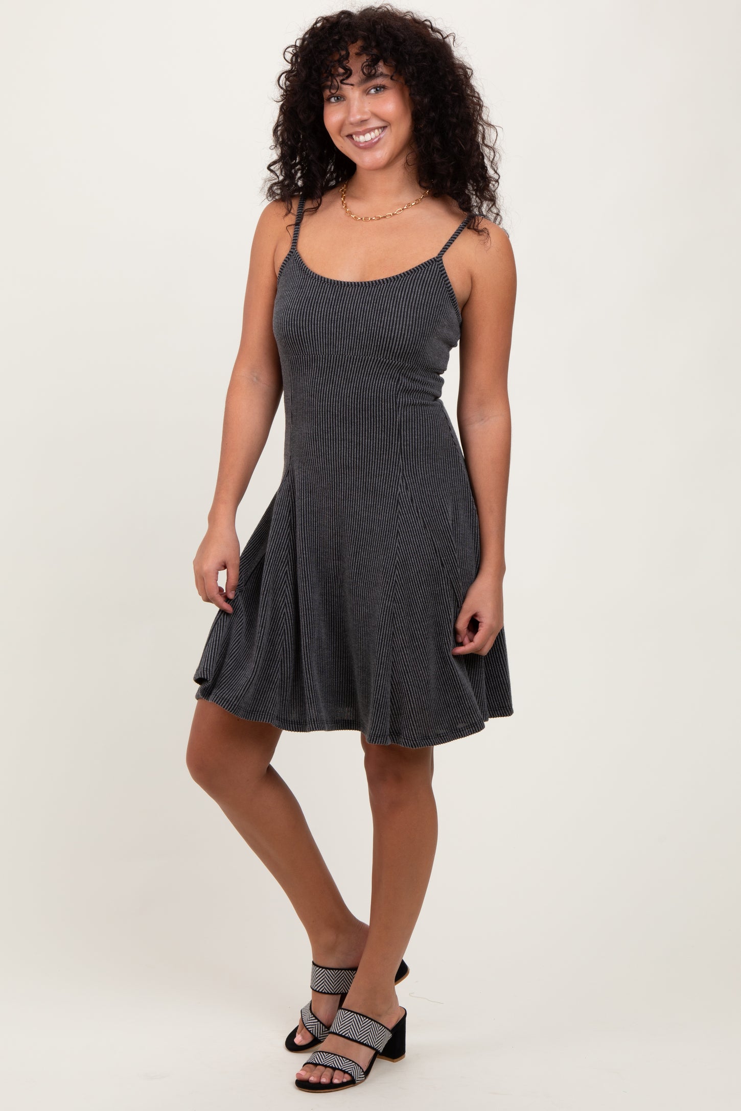 woman wearing a black and white striped mini dress with spaghetti straps and a flared skirt, standing with one leg slightly bent