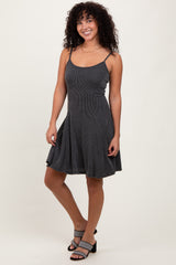 woman wearing a black and white striped mini dress with spaghetti straps and a flared skirt, standing with one leg slightly bent