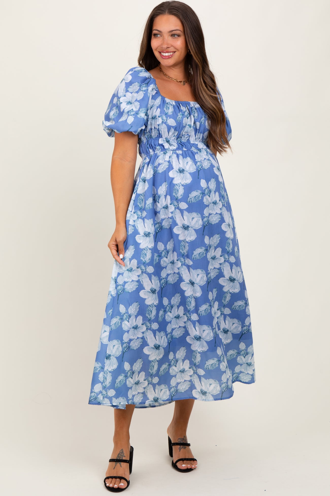 woman wearing a blue floral maternity maxi dress with puff sleeves and a gathered bodice, showing her baby bump