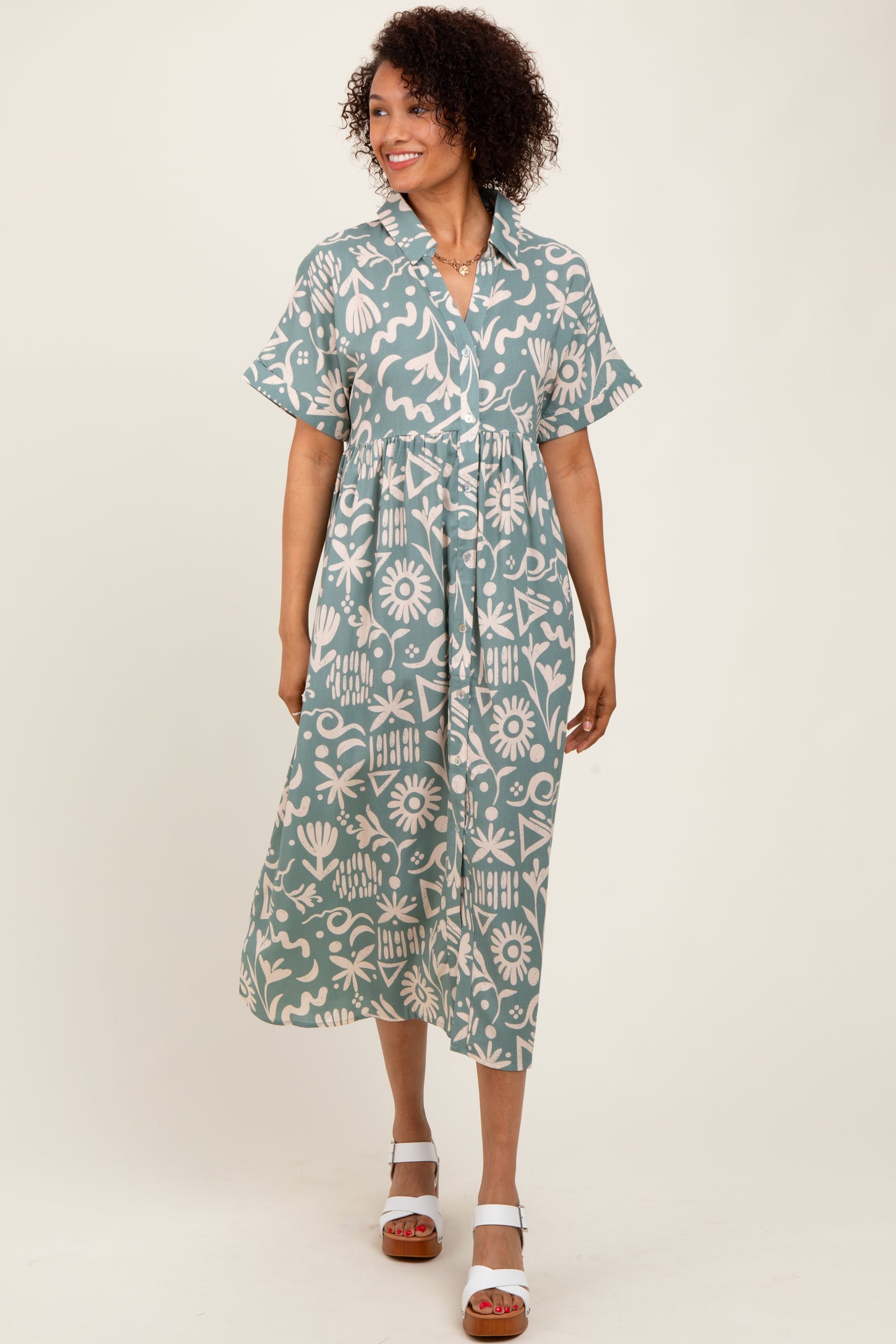 woman wearing a teal floral print midi shirt dress with short sleeves and a tie waist, standing on a neutral background
