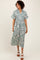 woman wearing a teal floral print midi shirt dress with short sleeves and a tie waist, standing on a neutral background