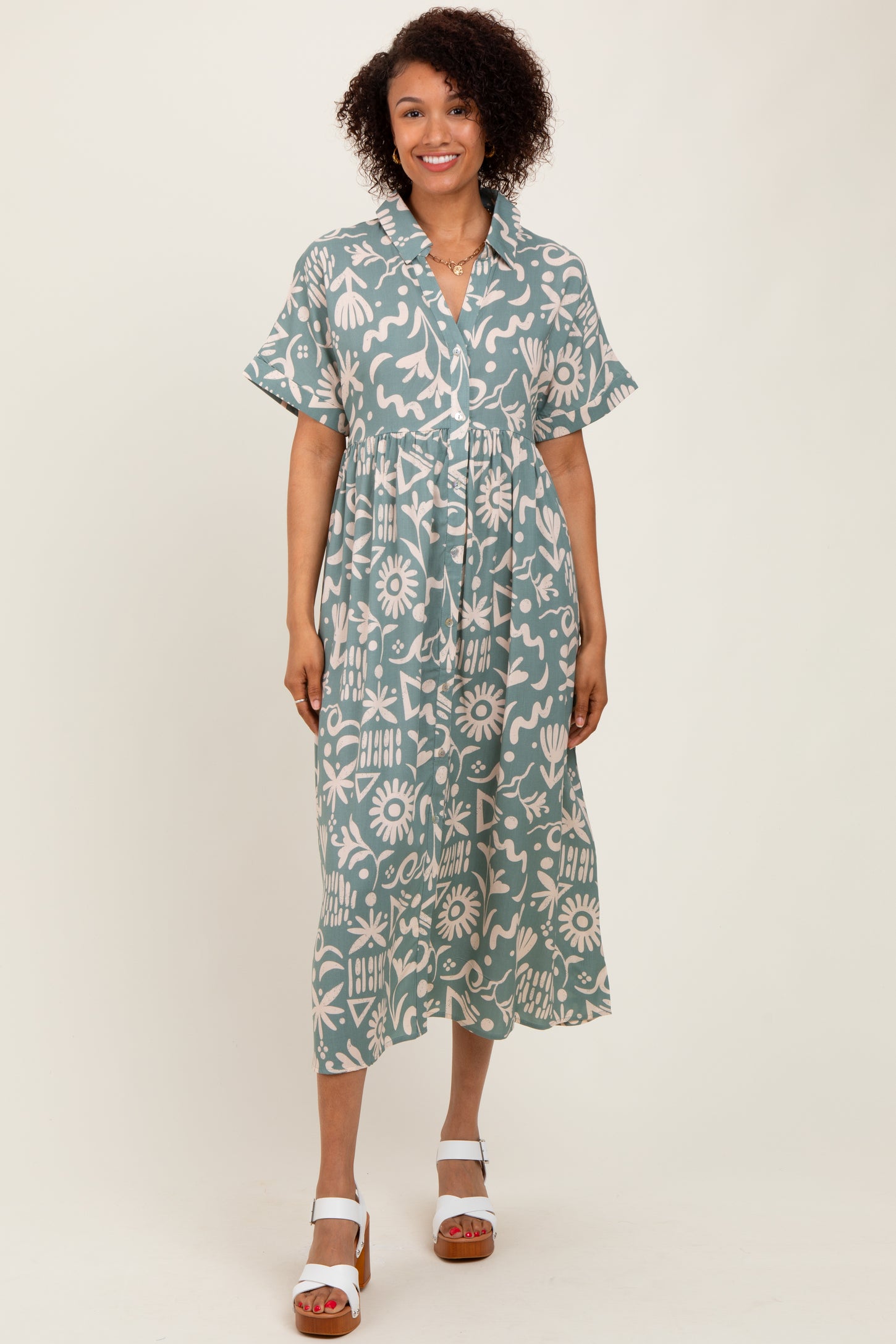 woman wearing a teal midi dress with a floral print and short sleeves, standing in a relaxed pose