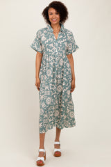 woman wearing a teal midi dress with a floral print and short sleeves, standing in a relaxed pose