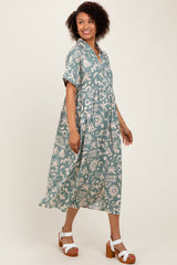 woman wearing a teal patterned midi dress with short sleeves and a cinched waist, standing in a side pose