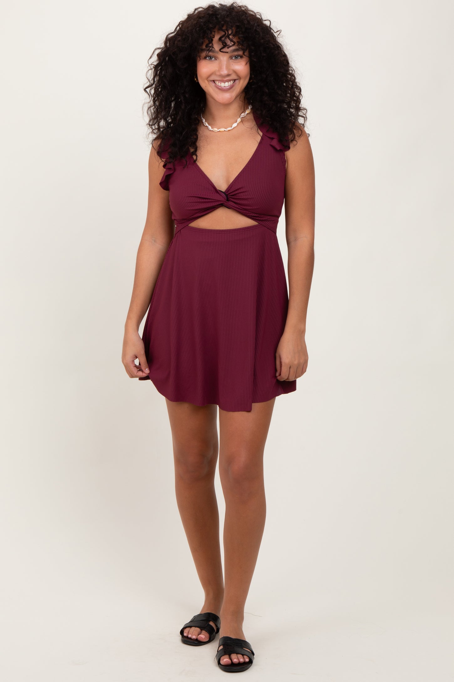 woman wearing a burgundy ruffled mini dress with a cutout detail and a flowy skirt, standing and smiling