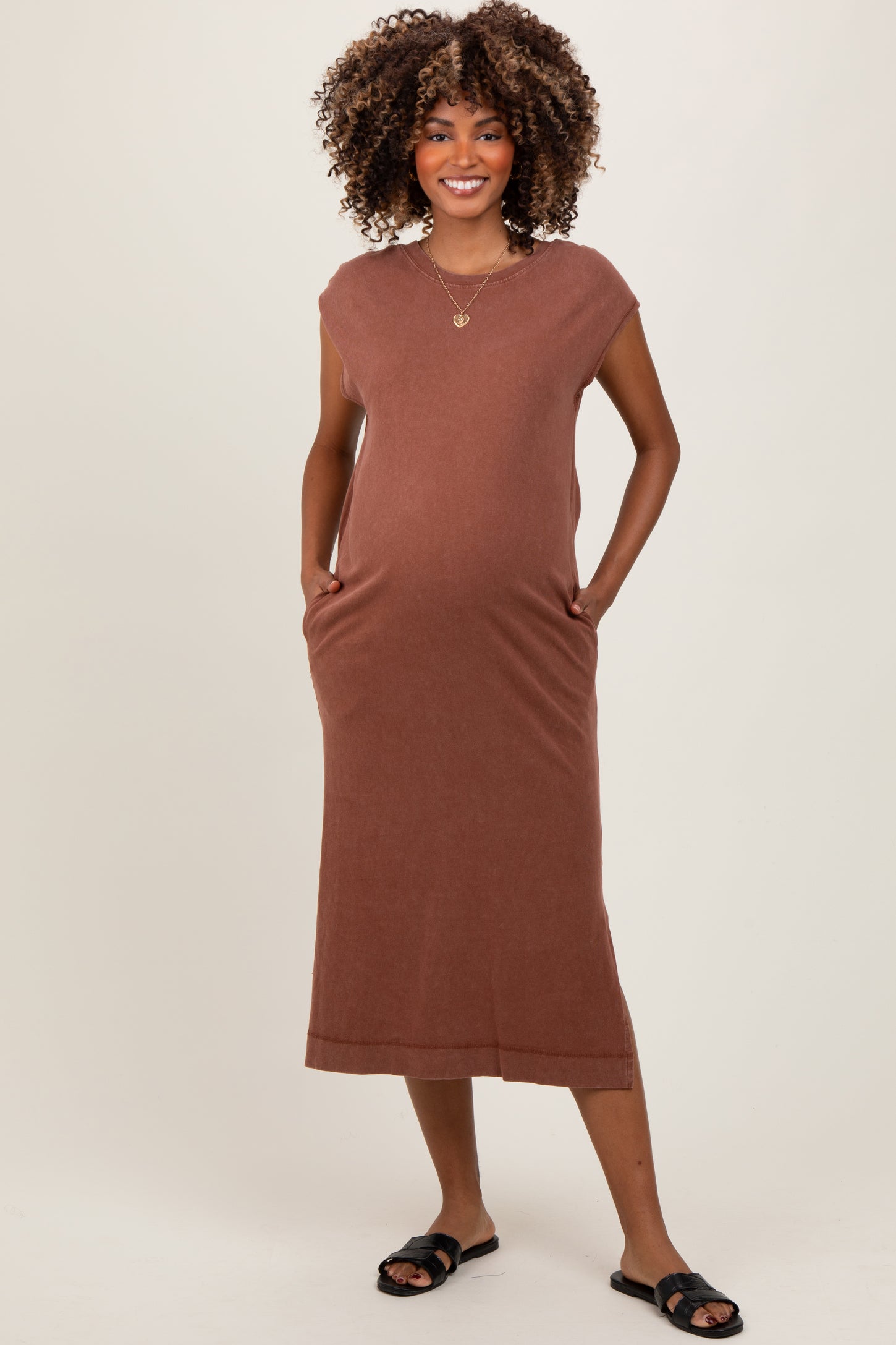 woman wearing a brown sleeveless maternity dress with pockets and a visible baby bump