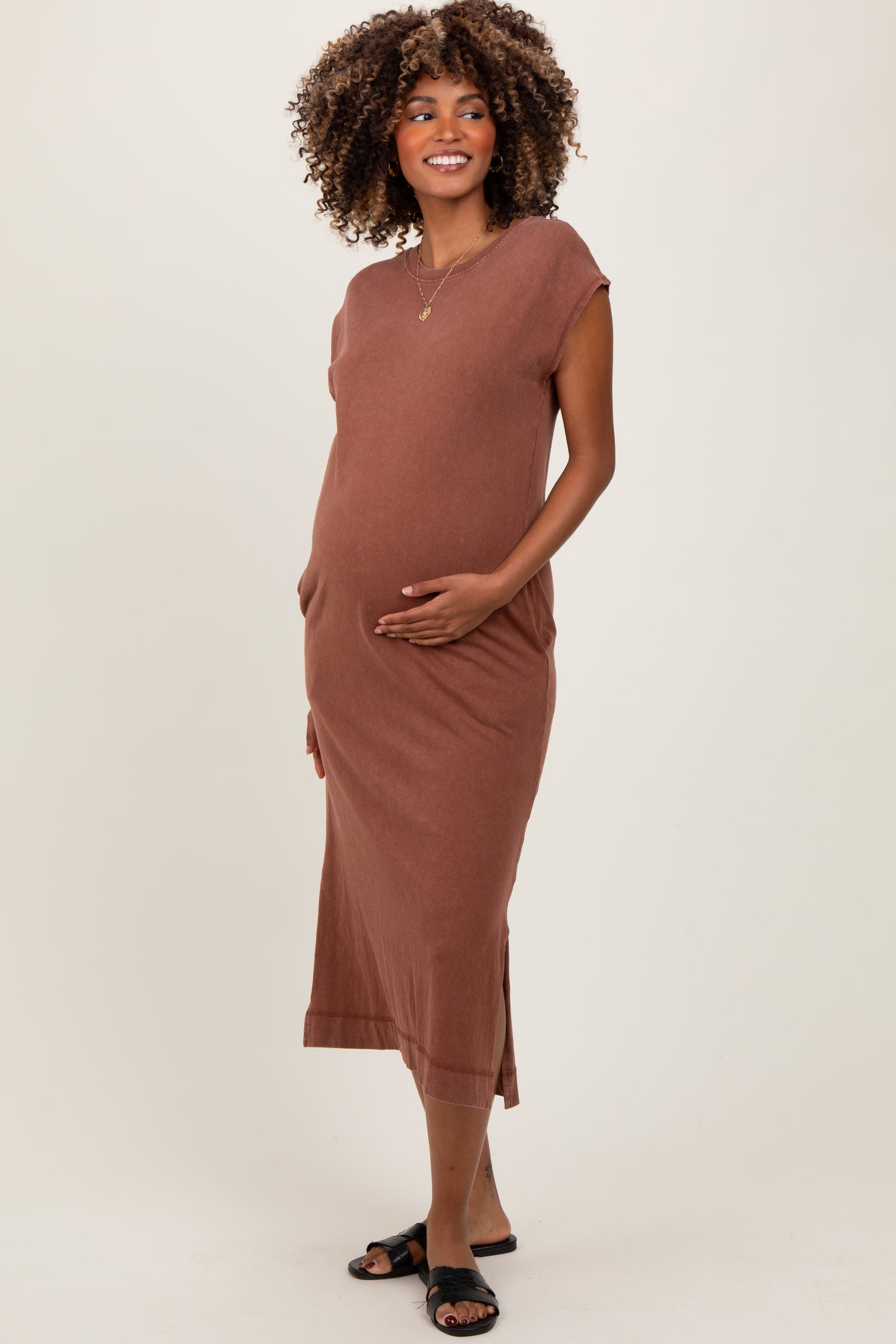 woman wearing a brown sleeveless maternity dress with side pockets and a visible baby bump