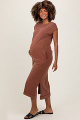 woman wearing a rust-colored maternity midi dress with short sleeves and side pockets, holding her baby bump