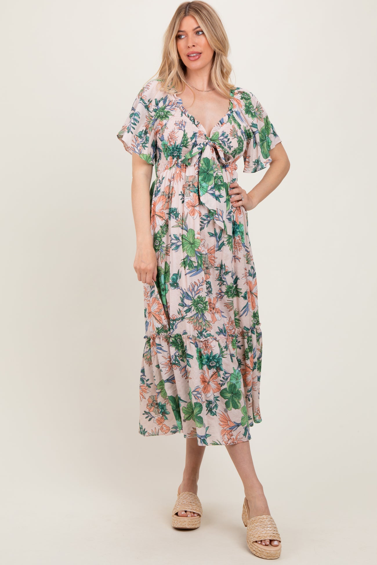 woman wearing a floral print maxi dress with short flutter sleeves and a tie front detail in a light pastel color