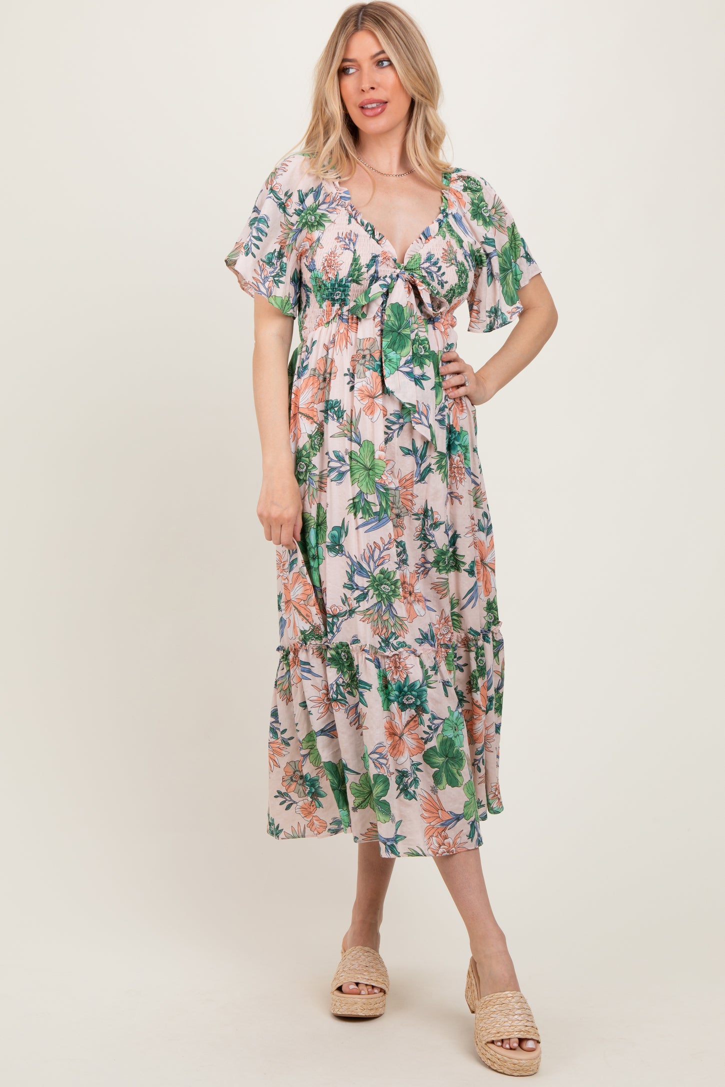 woman wearing a floral print maxi dress with short flutter sleeves and a tie front detail in a light pastel color