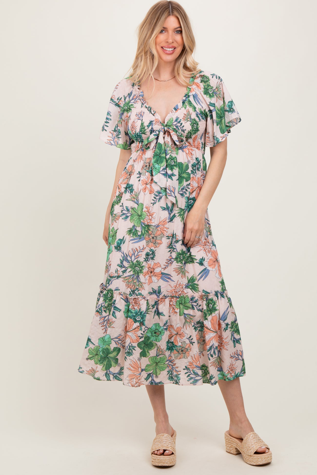 woman wearing a floral maxi dress with short sleeves and a tie-front detail, standing and smiling