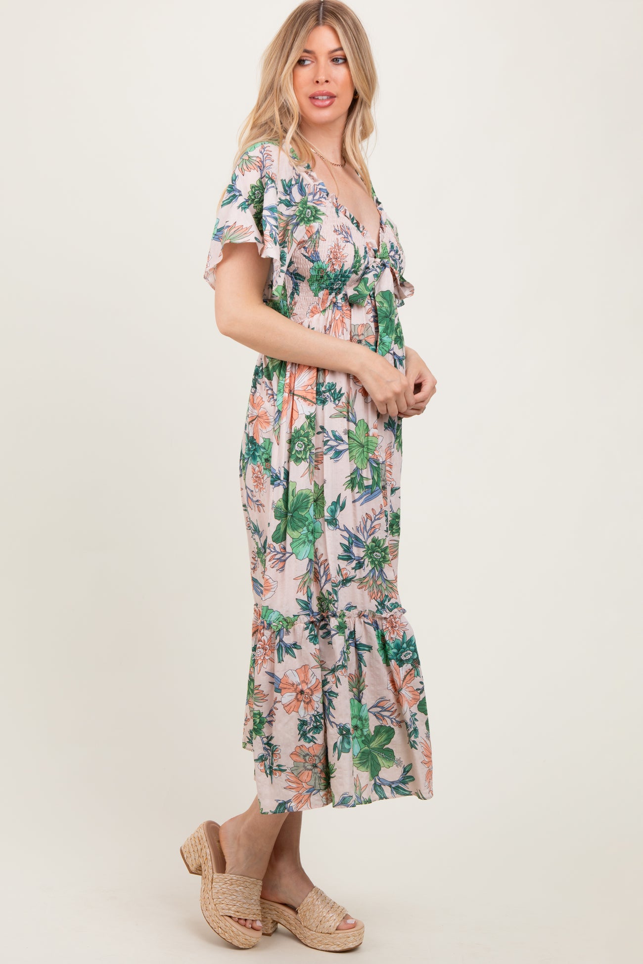 woman wearing a floral print maxi dress with flutter sleeves and a ruffled hem, standing sideways