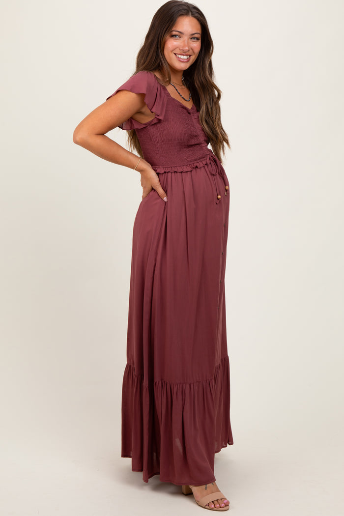woman wearing a burgundy maternity maxi dress with short ruffle sleeves and a smocked bodice, showing her baby bump