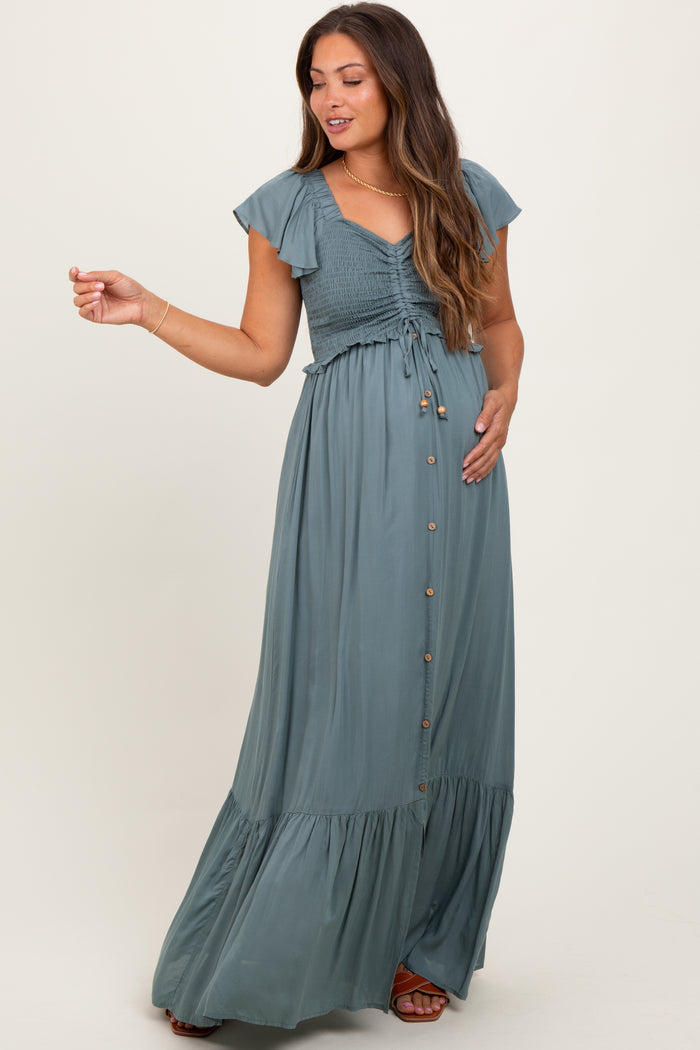 woman wearing a sage green maternity maxi dress with smocked bodice and button details, holding her baby bump