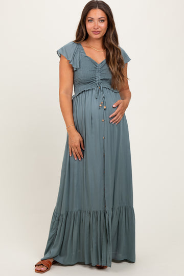woman wearing a slate green maternity maxi dress with ruffle sleeves, smocked bodice, and buttons, holding her baby bump
