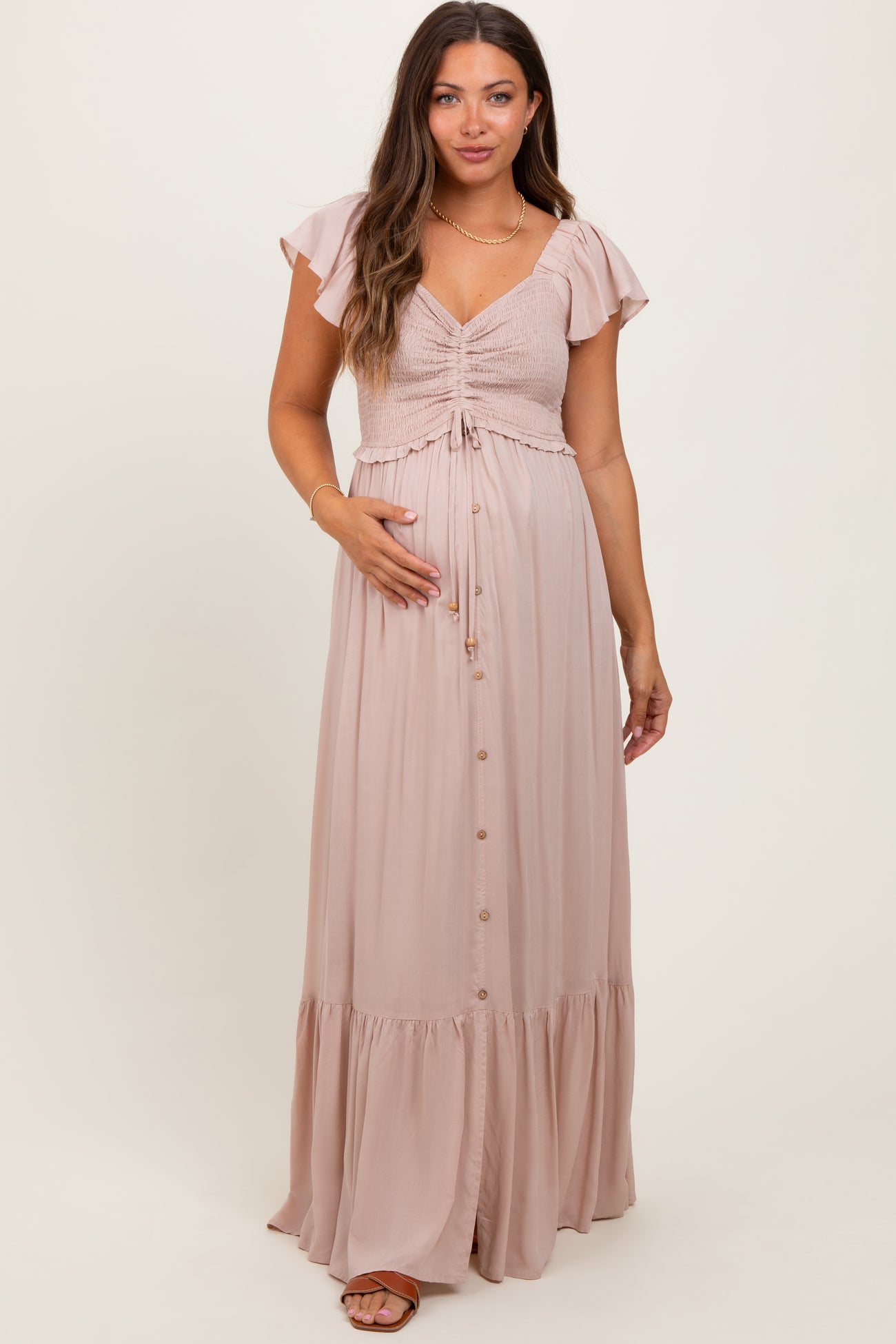 woman wearing a dusty pink maternity maxi dress with flutter sleeves and a cinched bodice, showcasing her baby bump