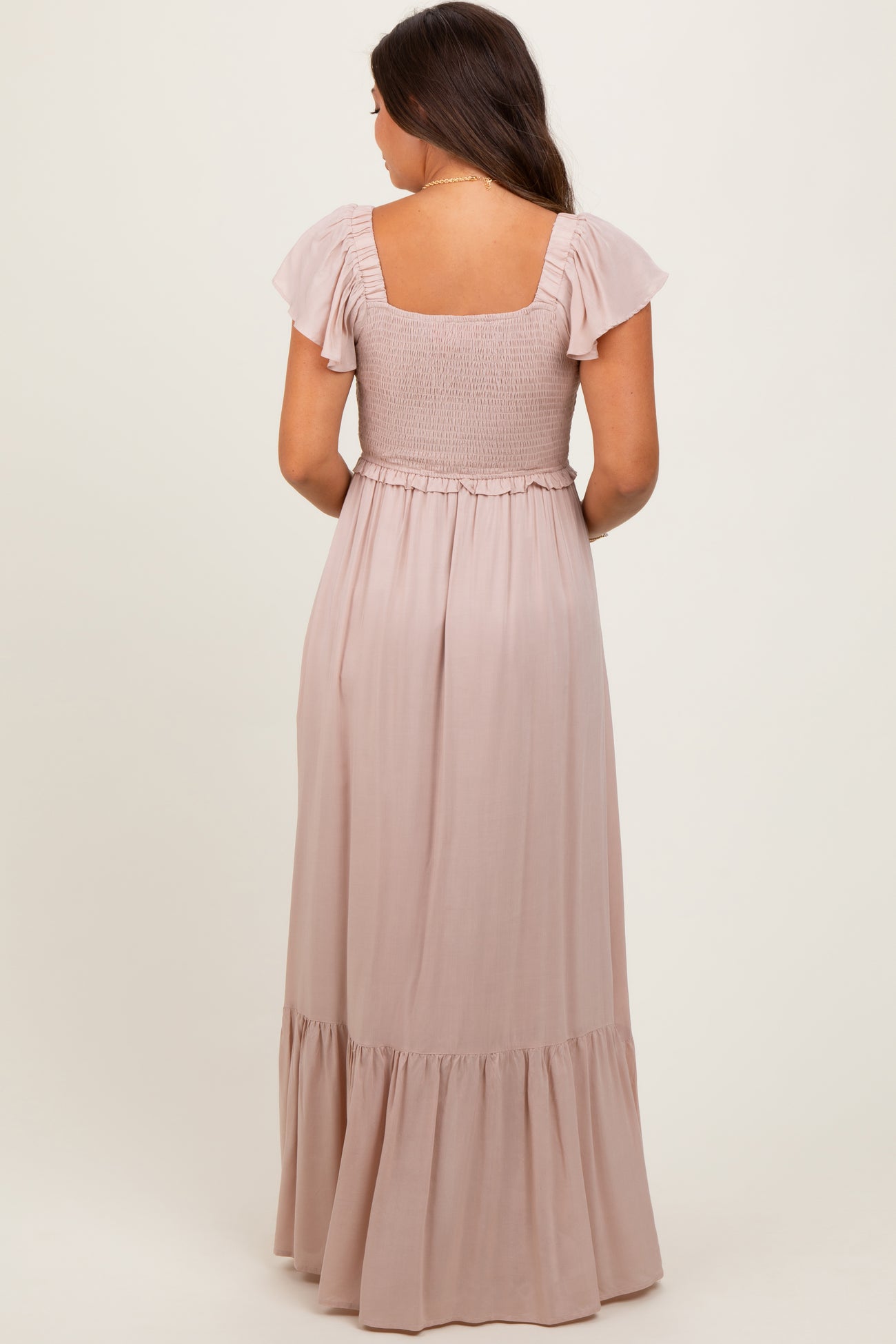 woman wearing a blush pink maternity maxi dress with smocked bodice and flutter sleeves, showing her baby bump