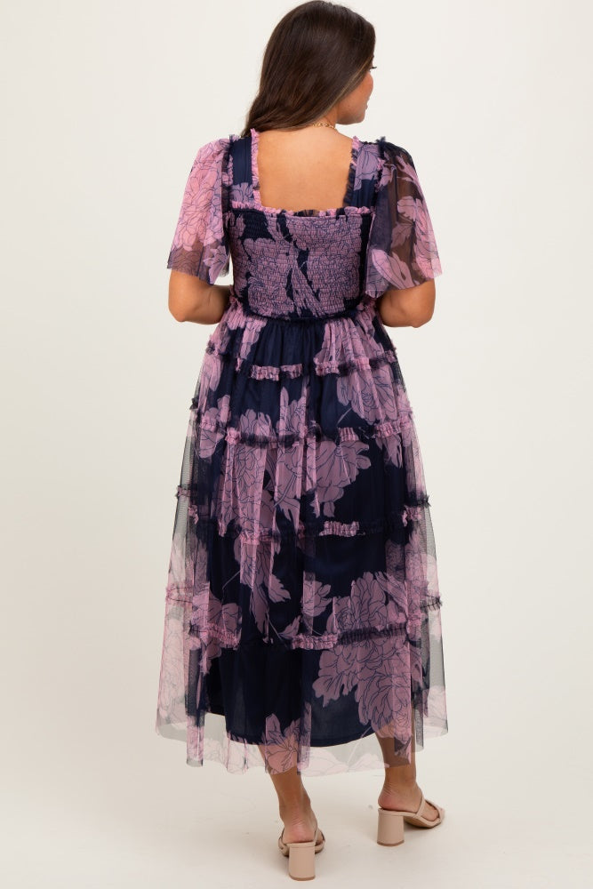 woman wearing a navy blue floral maternity dress with short puff sleeves and a tiered tulle skirt, showing her baby bump
