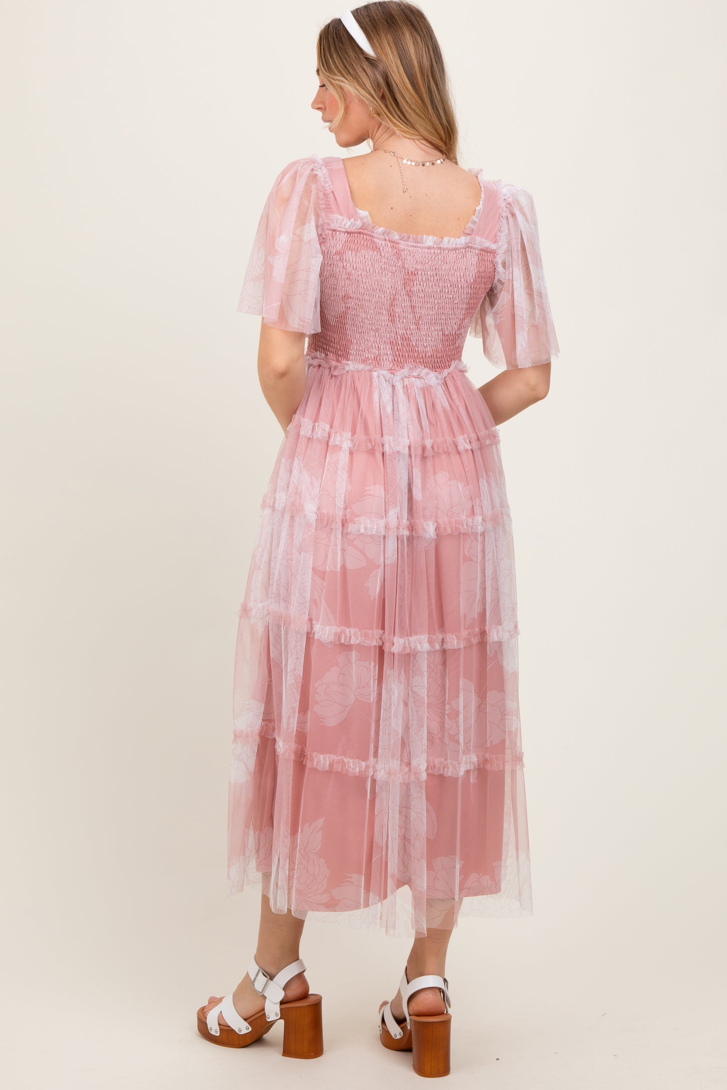 woman wearing a pink tiered midi dress with sheer short sleeves and floral patterns, viewed from the back