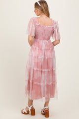 woman wearing a pink tiered midi dress with sheer short sleeves and floral patterns, viewed from the back