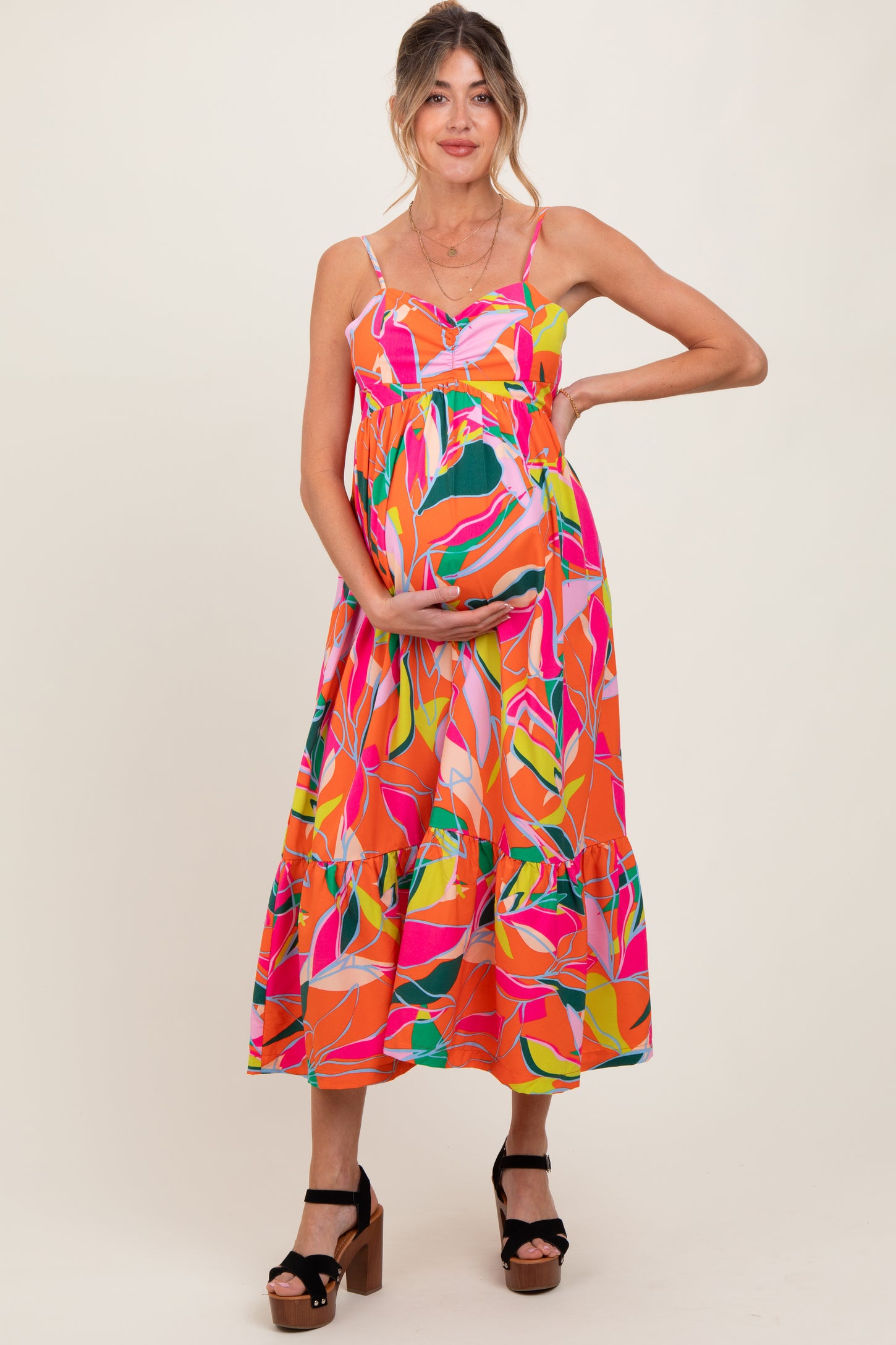 woman wearing a colorful floral maternity maxi dress with a baby bump and posing with one hand on her hip