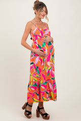 woman wearing a vibrant pink floral maternity dress with a ruffled hem and holding her baby bump