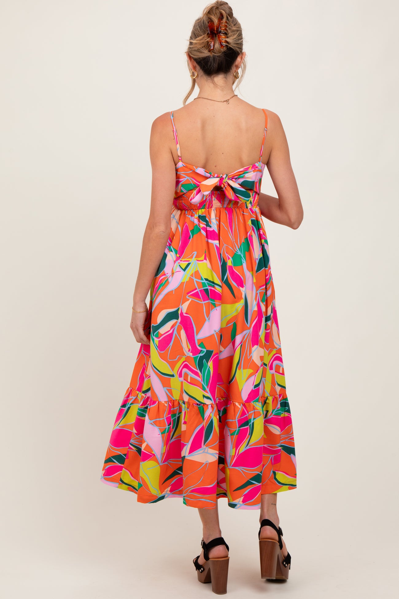 woman wearing a colorful floral print maternity dress with a tie-back detail and a flowy skirt