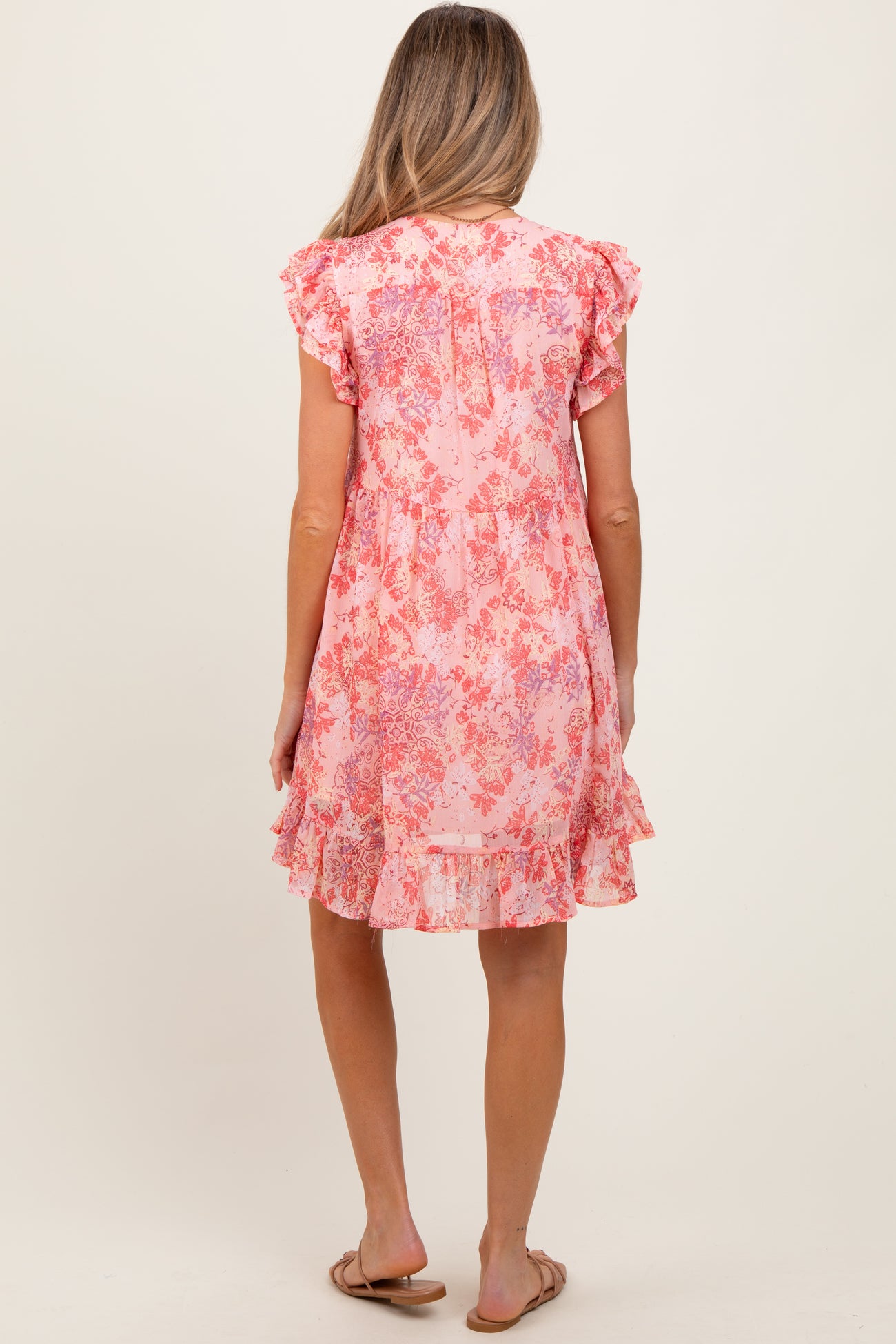 woman wearing a pink floral maternity dress with ruffled sleeves and a tiered hem, showing a baby bump from the back