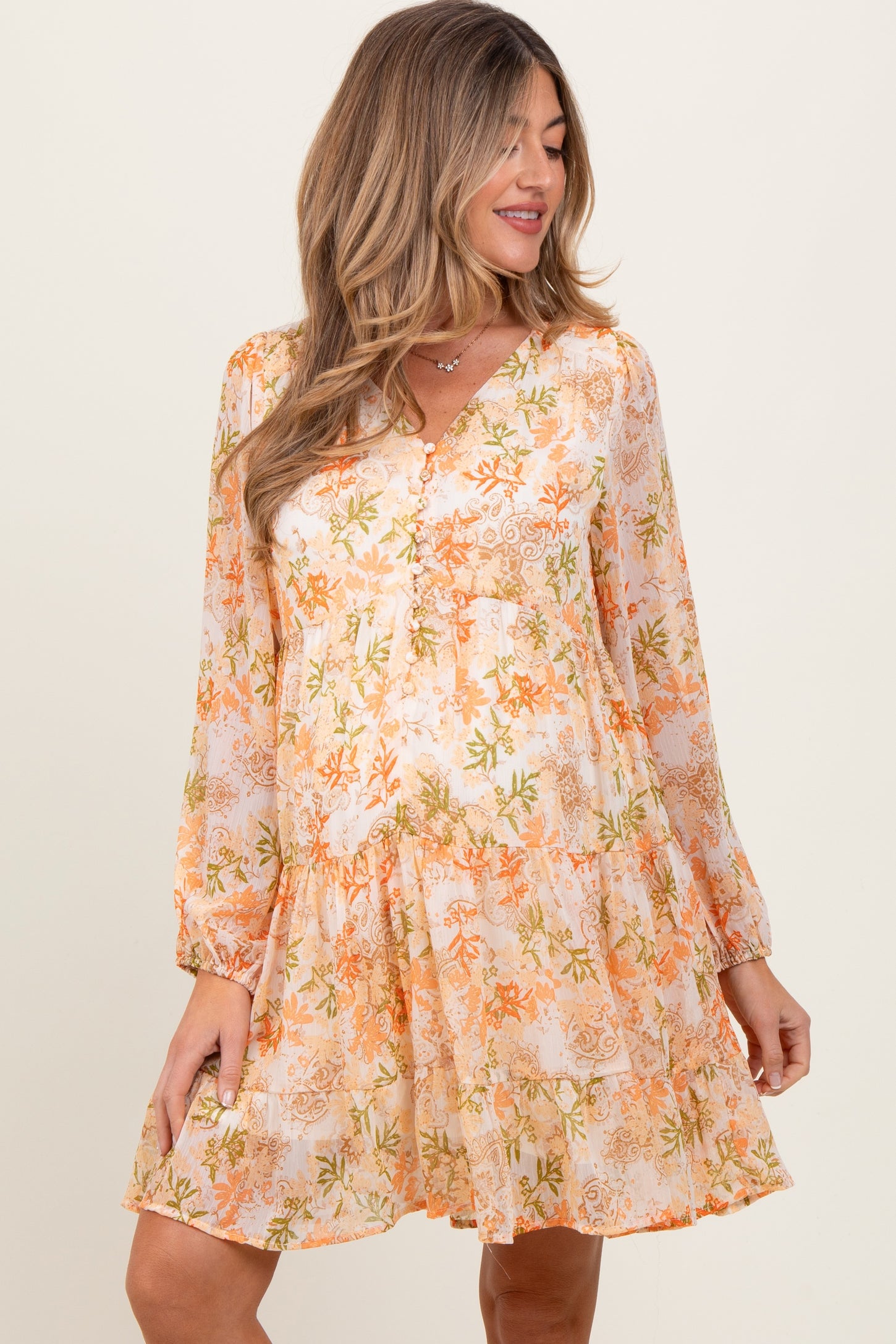 woman wearing a floral orange and white maternity dress with long sleeves and a tiered skirt, showing her baby bump