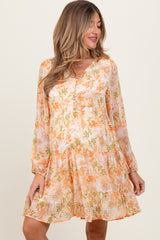woman wearing a floral orange and white maternity dress with long sleeves and a tiered skirt, showing her baby bump