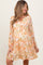 woman wearing a floral orange and white maternity dress with long sleeves and a tiered skirt, showing her baby bump