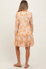 woman wearing a floral print short sleeve maternity dress in soft peach and orange tones, showing her baby bump