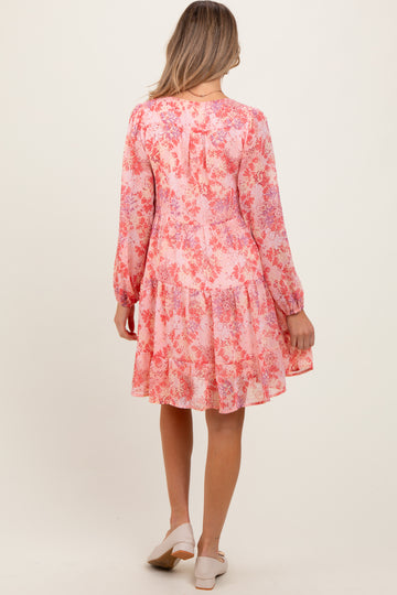 woman wearing a pink floral maternity dress with long sleeves and a tiered skirt, viewed from the back