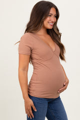 woman wearing a tan short sleeve maternity top and showing her baby bump while smiling