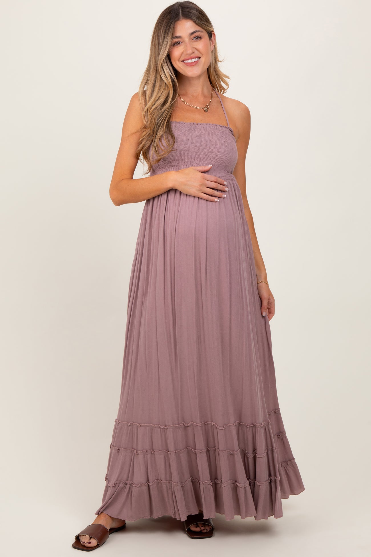 woman wearing a mauve maternity maxi dress with spaghetti straps and ruffled hem, holding her baby bump