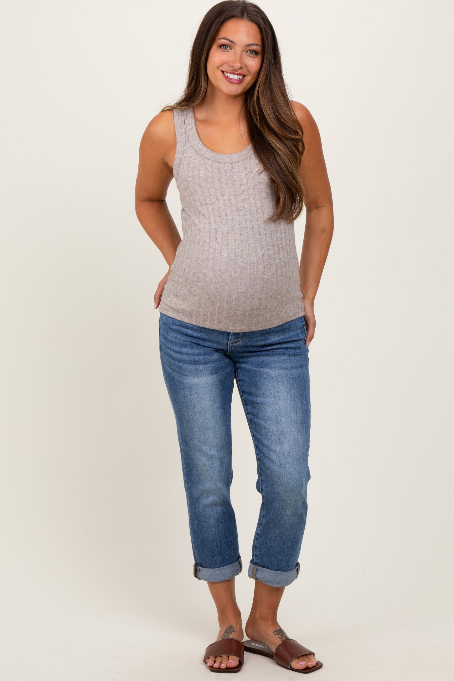 woman wearing a gray ribbed maternity tank top and blue rolled hem maternity jeans, showing her baby bump