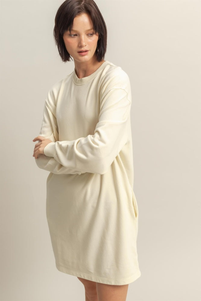 woman wearing a cream long sleeve oversized sweatshirt dress with side pockets