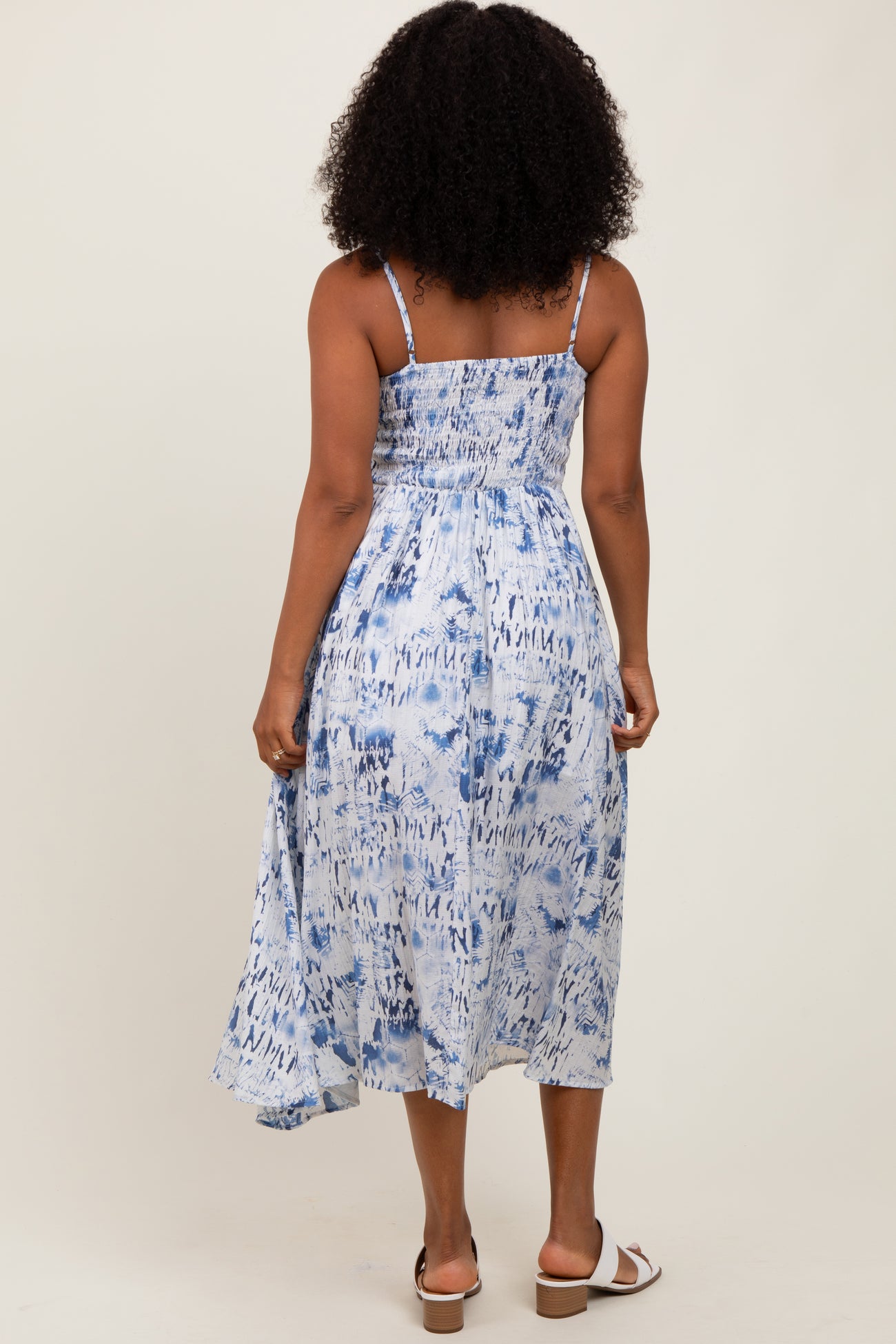 woman wearing a blue and white tie-dye midi dress with spaghetti straps and a smocked back, standing with her back to the camera