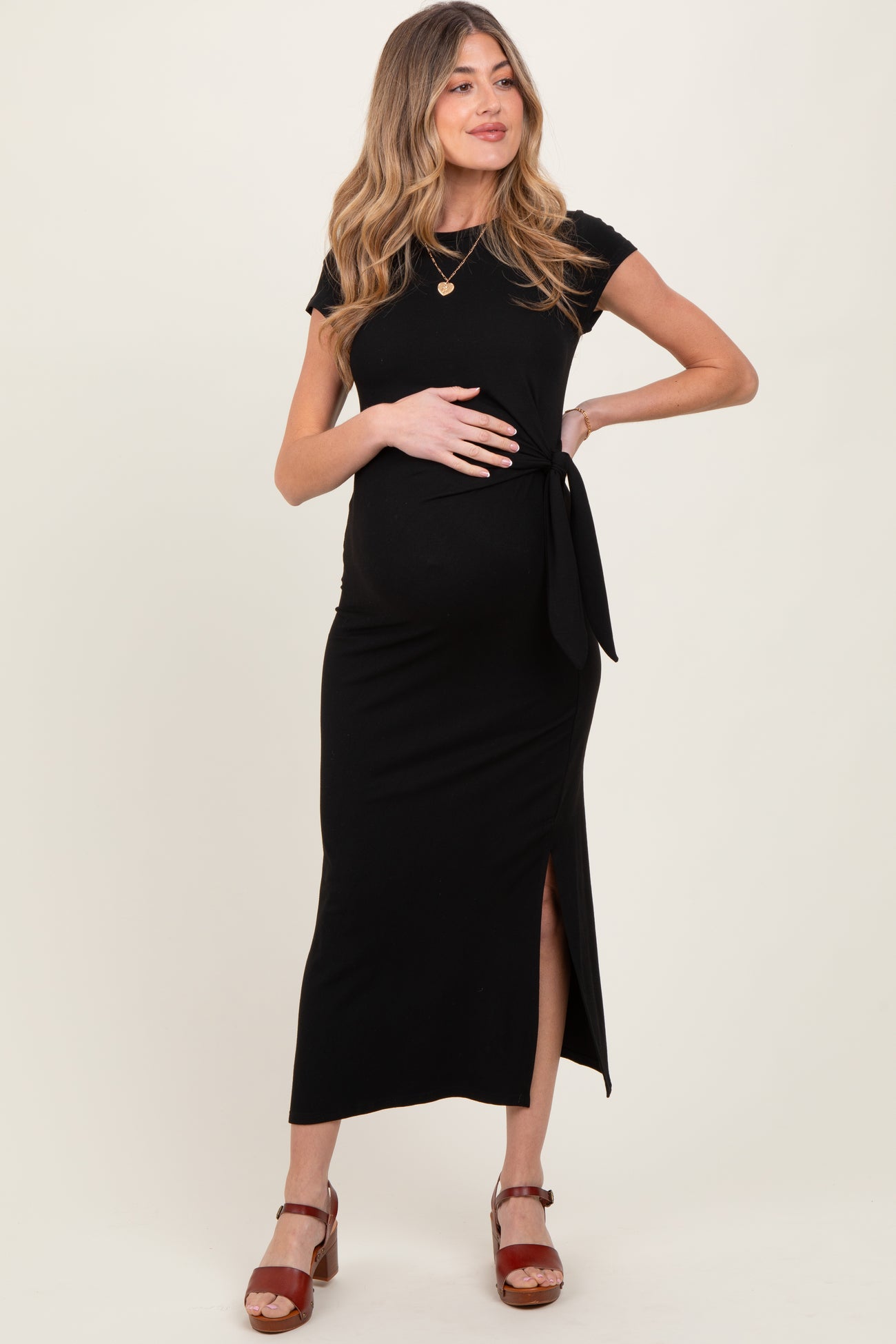 woman wearing a black maternity dress with a tie detail and side slit, showcasing her baby bump