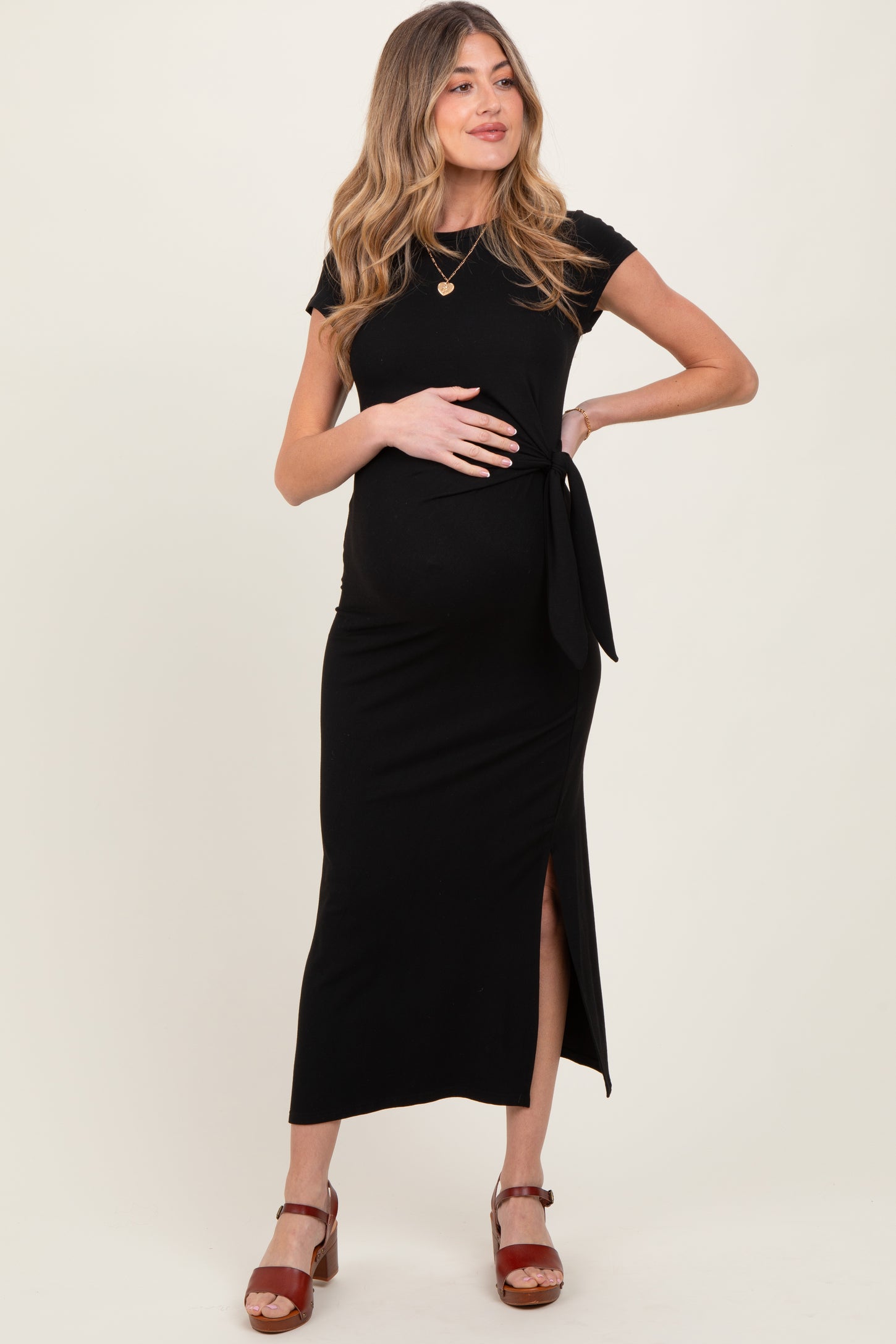 woman wearing a black maternity dress with a tie detail and side slit, showcasing her baby bump