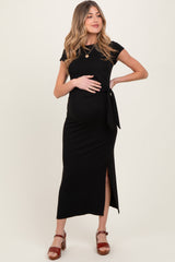 woman wearing a black maternity dress with a tie detail and side slit, showcasing her baby bump