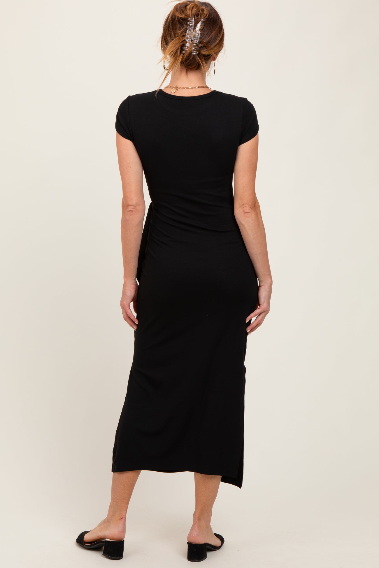 woman wearing a black cap sleeve maxi dress, showing a fitted silhouette and a side slit, viewed from the back