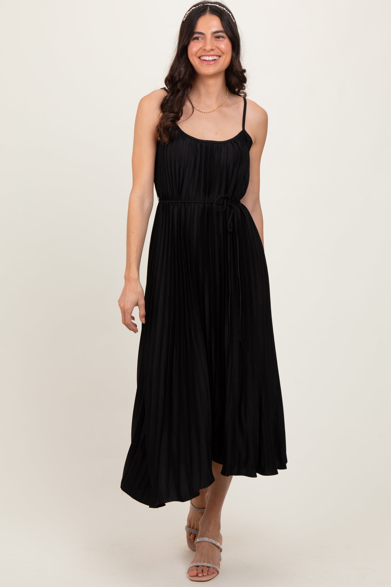woman wearing a black pleated midi dress with spaghetti straps and a tie waist detail