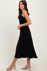 woman wearing a black pleated midi dress with thin straps and styled with clear strap sandals
